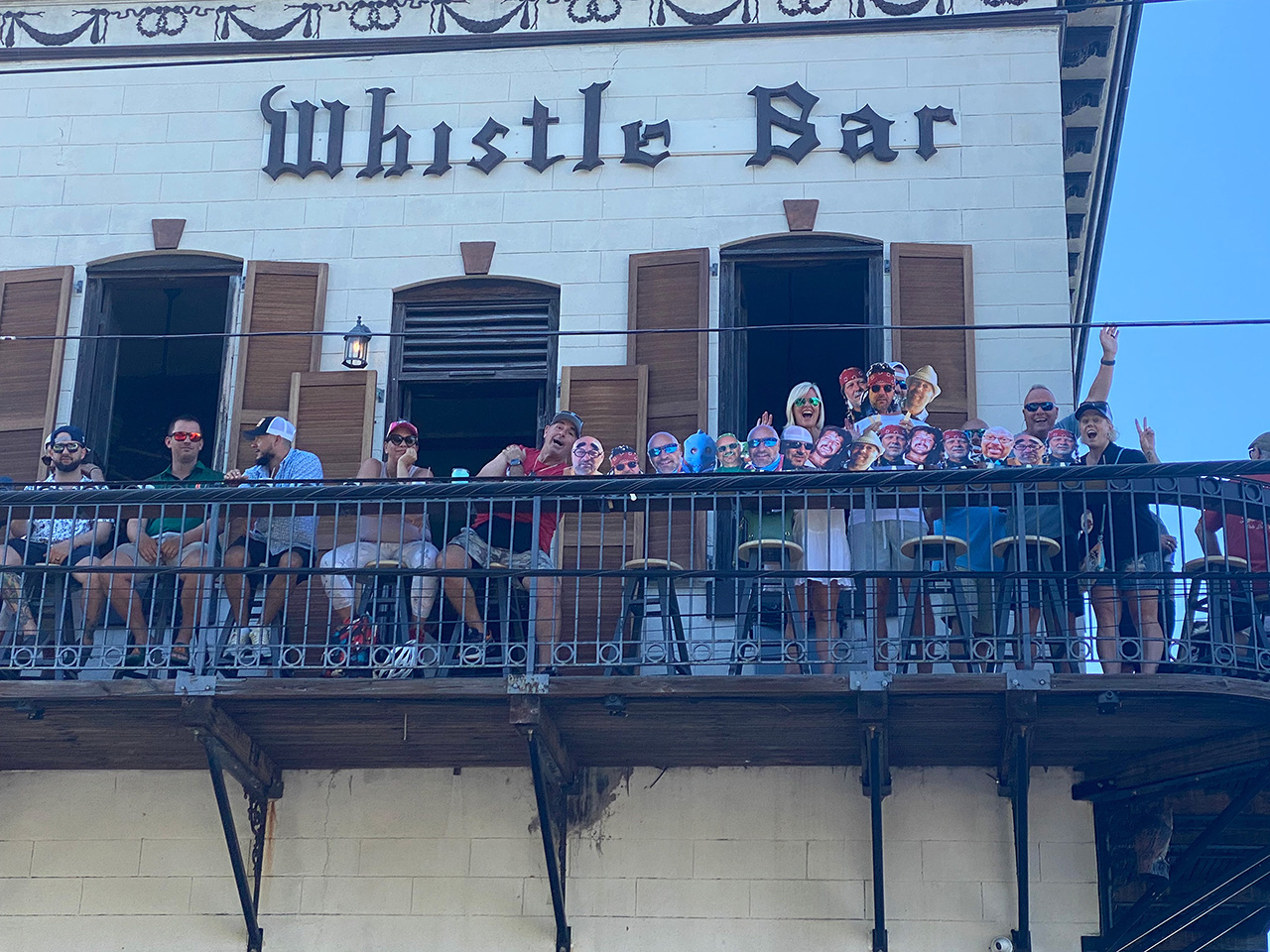 People in Key West smiling and waving on an upper-level bar patio